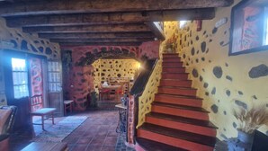 A rustic interior with a stone wall, a wooden staircase, and a dining area.