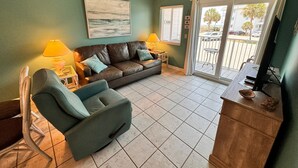 A living room with a sofa, a chair, a TV, and a balcony with a view of the street. - Gulf Shores Plantation (Gulf Shores)