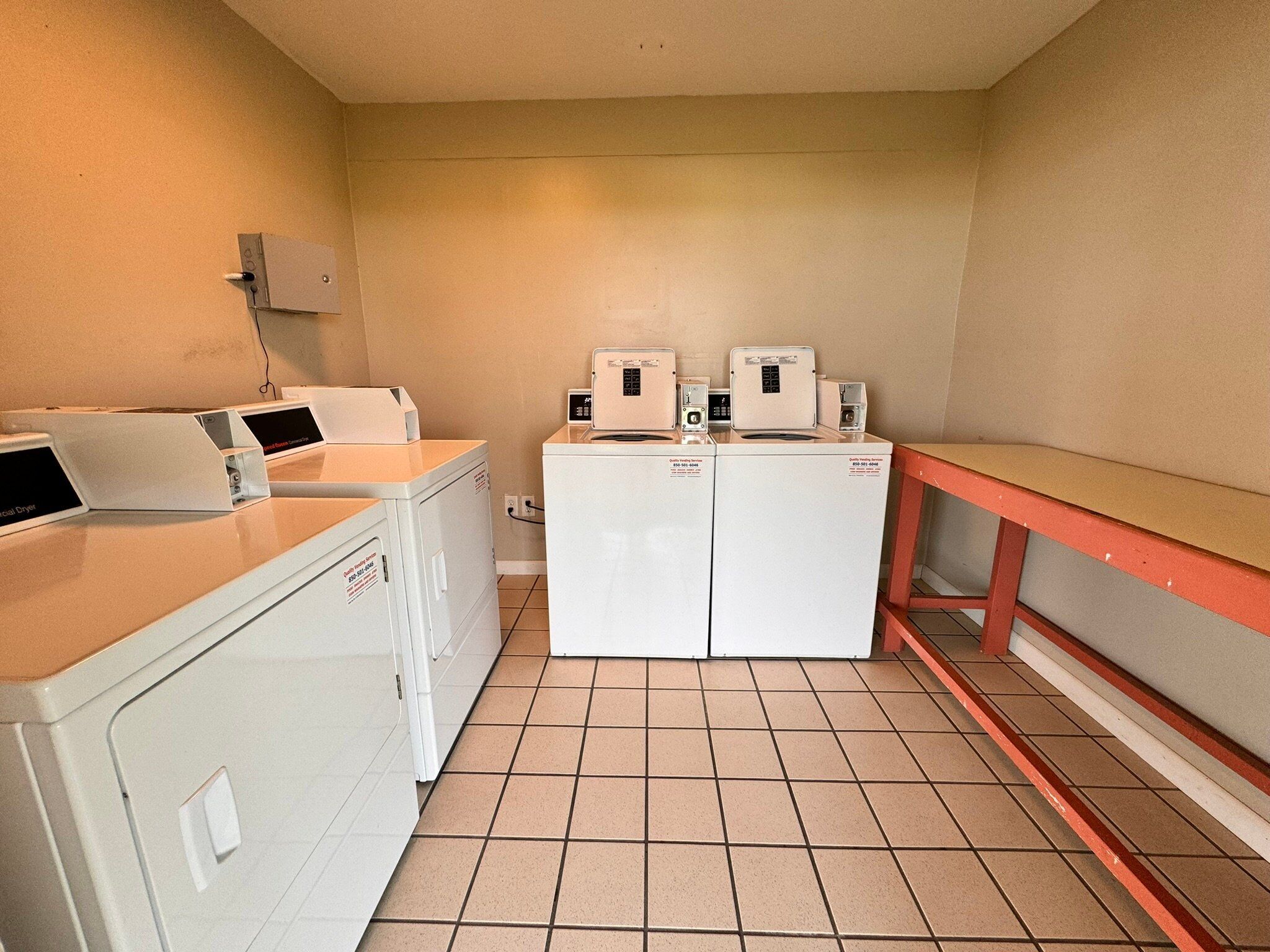 A laundry area with a washing machine, dryer, and a small table with a red bench.