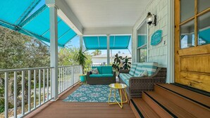 Eine überdachte Veranda mit Korbmöbeln, einem kleinen runden Tisch und einem Blumentopf.