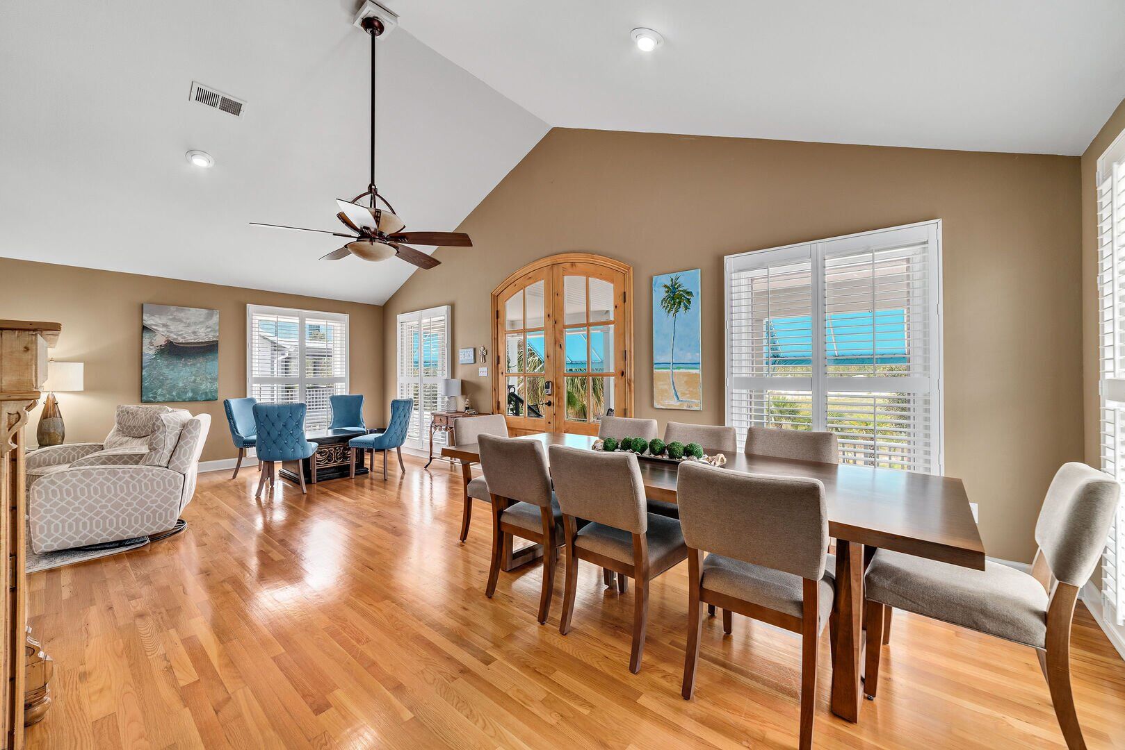 A spacious living room with a wooden dining table, blue chairs, and a ceiling fan.