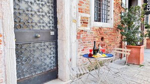 Un bâtiment rustique avec une porte en métal, une petite table sur laquelle se trouvent une bouteille et des verres, et un banc.