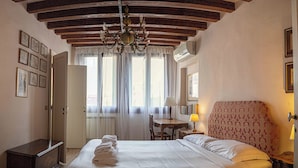 Una camera d'albergo con un letto grande, un soffitto in legno, un lampadario, una scrivania con una lampada e una finestra con tende.