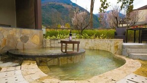 A hot tub with a stone border, a table with a bottle, and a view of mountains. - Gongga cliff Hot Spring Hotel (Luding)