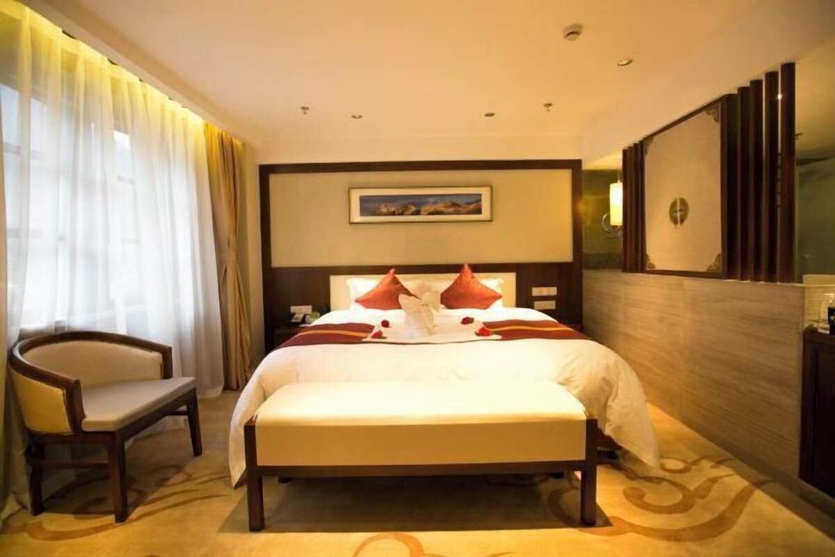 A hotel room with a large bed, a chair, a painting on the wall, and a TV on the wall.