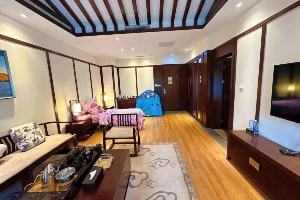 Habitación de hotel con suelo de madera, sofá, mesa de comedor con sillas, televisor y ventana grande.
