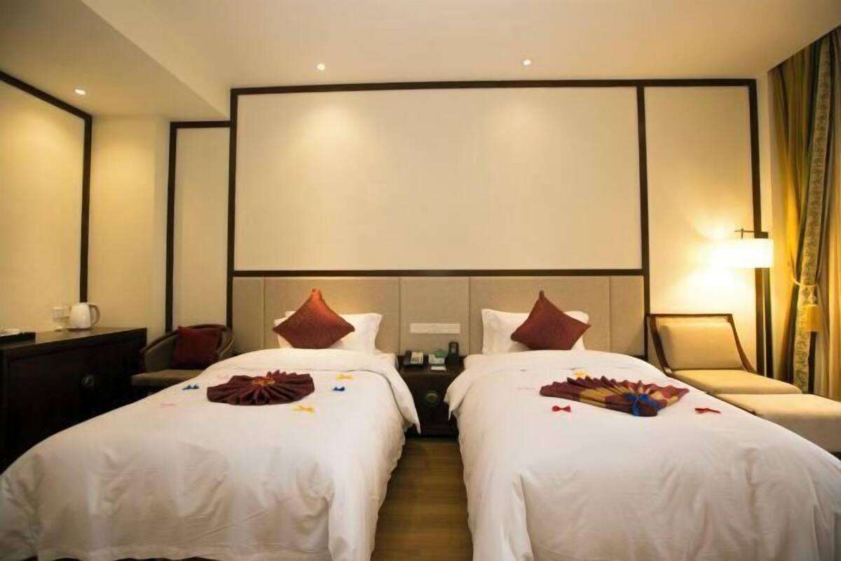 Habitación de hotel con dos camas, un televisor grande montado en la pared, un escritorio con lámpara y una silla.