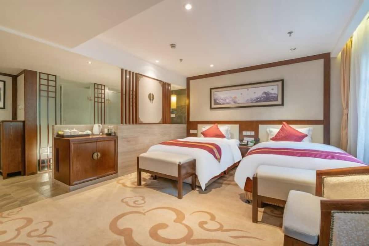 Habitación de hotel con dos camas, un armario de madera, un espejo grande y una obra de arte enmarcada en la pared.