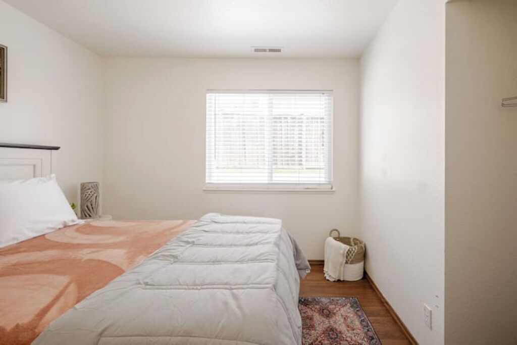 Ein Schlafzimmer mit Bett, Fenster mit Jalousien, Nachttisch und Teppich.