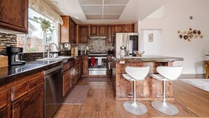 Eine Küche mit Holzschränken, einer zentralen Kochinsel mit Barhocker, einer Stein-Spritzschutzwand und einem Edelstahl-Kühlschrank.