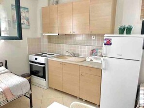 Compact kitchen with a stove, refrigerator, sink, and small window.