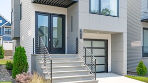 Un edificio moderno de dos pisos con una escalera que lleva a la puerta principal, un pequeño porche y una vista despejada del vecindario.