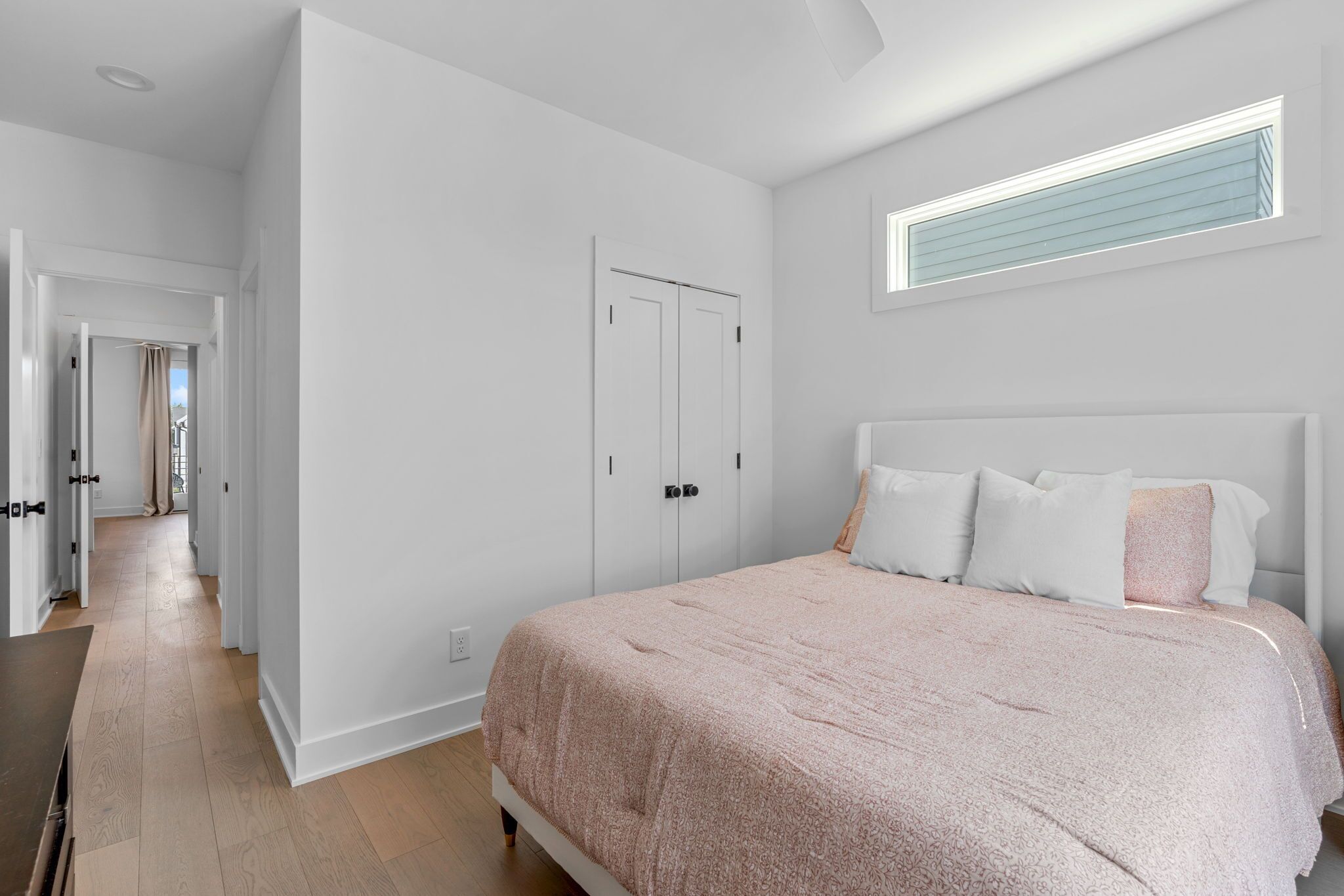 A bedroom with a large bed, white walls, a wardrobe, and a window with blinds.