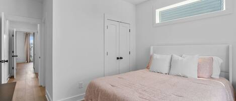 A bedroom with a large bed, white walls, a wardrobe, and a window with blinds.