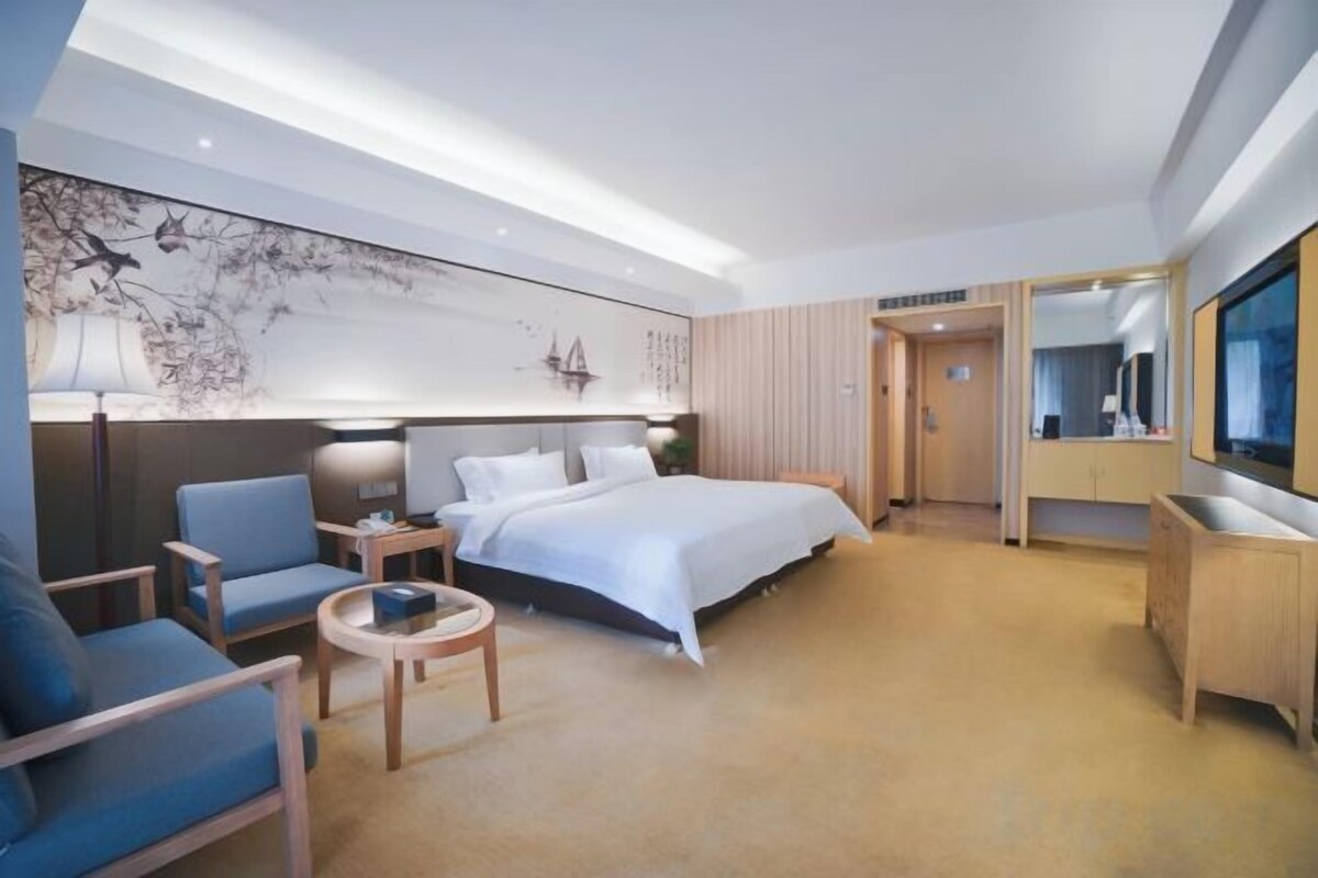 Ett hotellrum med en säng, ett skrivbord, en stol, ett litet bord och ett stort konstverk på väggen.