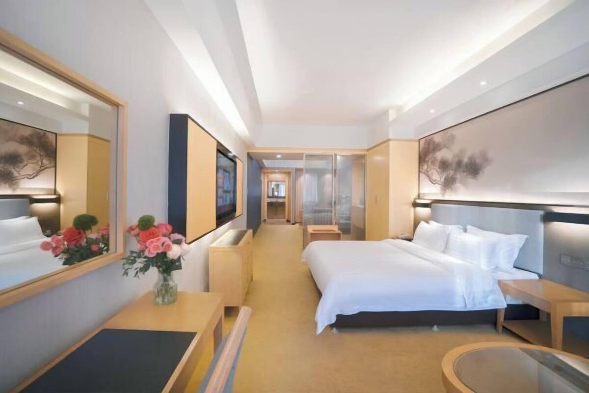 A modern hotel room with a large bed, a bedside table, a mirror, and a view of the hallway.