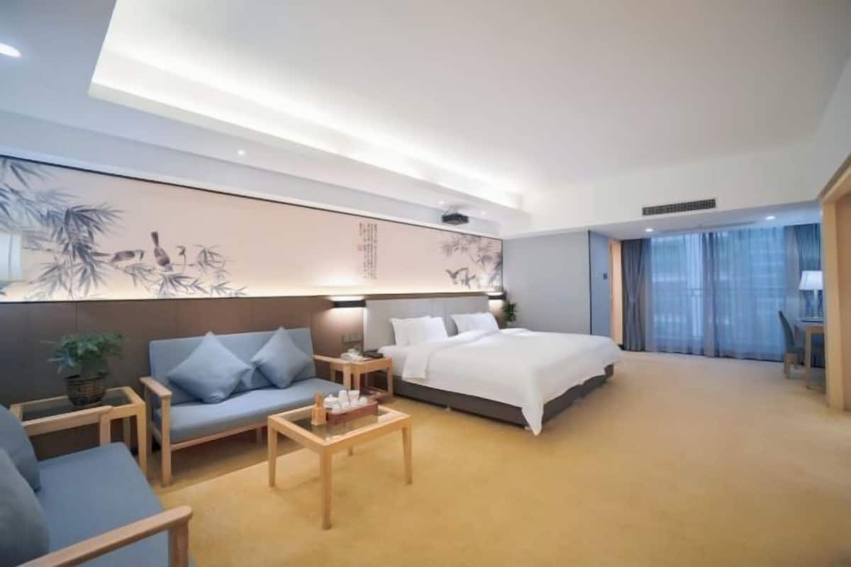 A modern hotel room with a large bed, a sofa, a coffee table, and a wall with artwork.