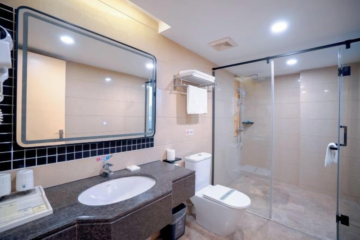 A modern bathroom with a large mirror, a sink, a toilet, and a glass-enclosed shower.