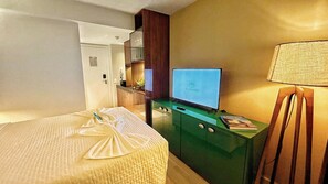 Una habitación de hotel con una cama, televisión, escritorio con lámpara y un mini bar.