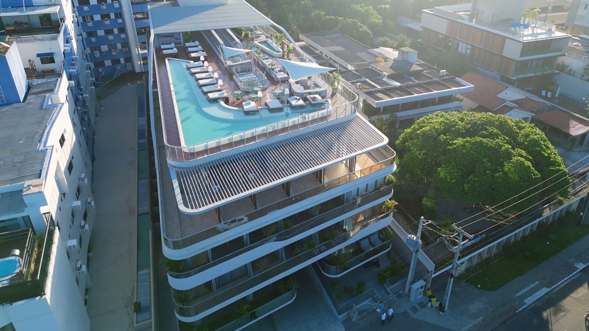 Um hotel moderno com piscina no terraço, várias varandas e vista para a área urbana circundante.