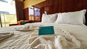 A neatly made bed with a white comforter and pillows, a teal sign with text, and a view of the outside through a window. - Setai Yacht Prime - By Almare (João Pessoa)