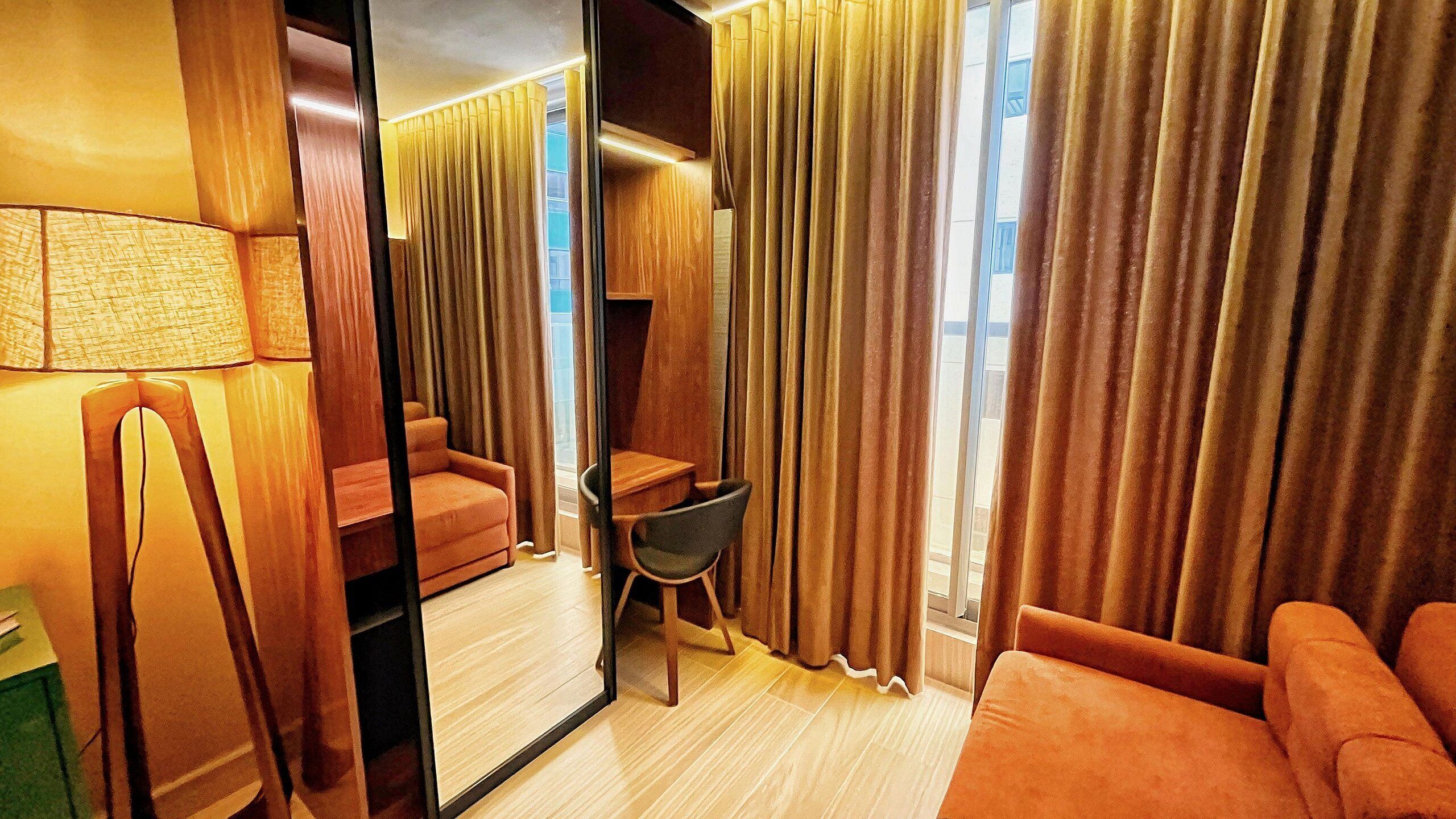 Habitación de hotel con un espejo grande, un sofá, una silla y un escritorio.