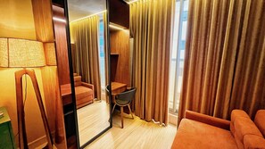 A hotel room with a large mirror, a sofa, a chair, and a desk.