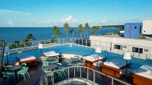 Un espace piscine aménagé sur le toit, avec des chaises longues et des tables, offrant une vue sur l’océan.