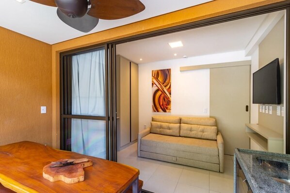A modern room with a wooden table, a sofa, a ceiling fan, and a TV.
