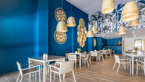Un interior de restaurante moderno con paredes azules, muebles blancos y lámparas de mimbre colgantes.