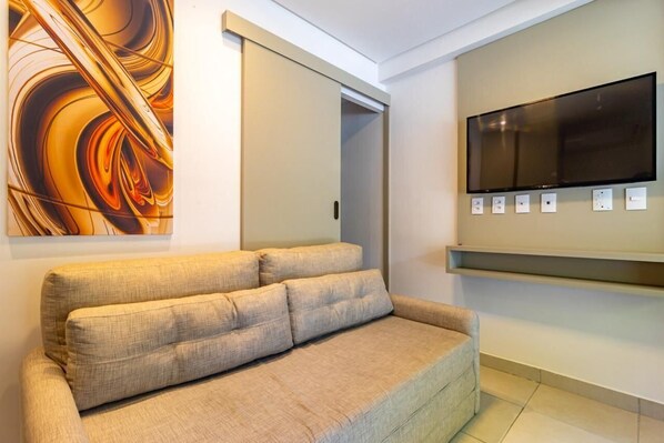 A modern living room with a beige sofa, a flat-screen TV mounted on the wall, and a sliding door.