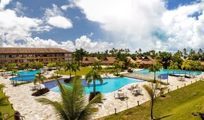A resort with multiple swimming pools, palm trees, and a large building in the background.