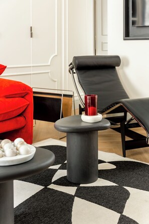 Una sala moderna con un sofá rojo, un sillón negro, una mesita redonda con una vela roja y una alfombra estampada.