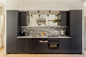 Una cocina moderna con encimera de mármol, armarios negros y horno empotrado.