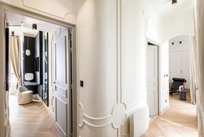 Un pasillo moderno de hotel con paredes blancas, suelo de madera y una zona de estar con una silla y una mesita.