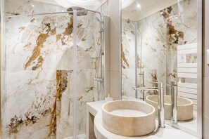 Ein modernes Badezimmer mit einer gläsernen Duschkabine, Marmorwänden und einem runden Waschbecken.