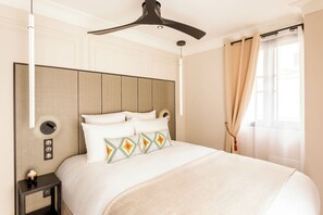 Een hotelkamer met een groot bed, een plafondventilator, een nachtkastje en een raam met gordijnen.