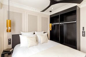A hotel room with a large bed, two bedside tables, a black wardrobe, and a ceiling light fixture.