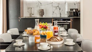 Une table mise pour le petit-déjeuner, avec une nappe pour deux personnes, comprenant des croissants, des fruits, du jus de fruits et un panier de pain.
