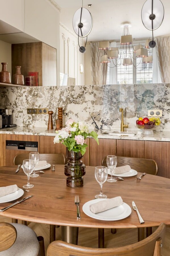A dining area with a wooden table set for four, a vase with flowers, and a marble backsplash.