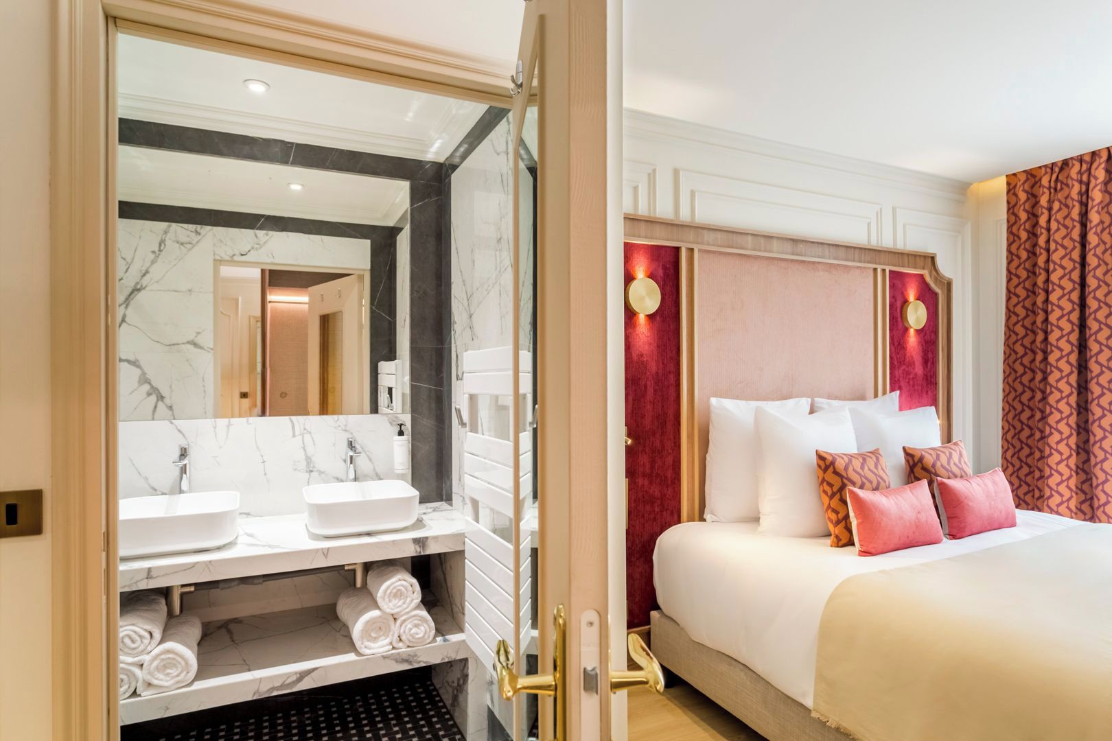 A hotel room with a marble bathroom vanity, a bed with multiple pillows, and a red accent wall.
