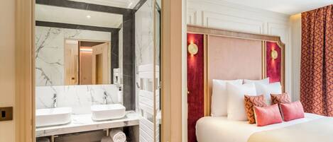 A hotel room with a marble bathroom vanity, a bed with multiple pillows, and a red accent wall.