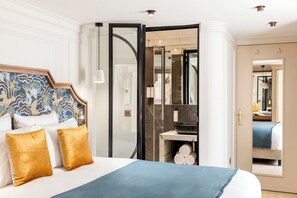 Une chambre d’hôtel avec un grand lit, une salle de bain dotée d’une douche à parois de verre et un miroir qui reflète la pièce.