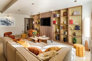 A modern living room with a sofa, coffee table, and a television. There are bookshelves with decorative items and a fireplace. - Merveil - Signature Suite - Marais - Archives II (Paris)