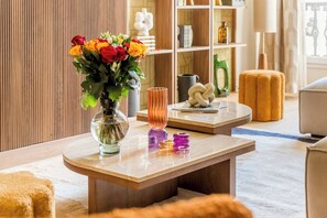 Un salon moderne avec un plancher en bois, une table basse ronde, un vase rempli de fleurs et une bibliothèque en arrière-plan.