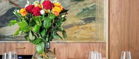 Una mesa de comedor dispuesta con platos, cubiertos y copas de vino, con un florero en el centro.
