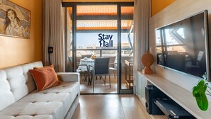 A hotel room with a sofa, a flat-screen TV, a dining table with chairs, and a sliding glass door leading to an outdoor area.