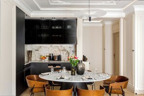 A modern dining area with a marble table, wooden chairs, and a kitchen in the background.