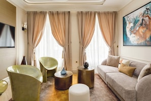 A modern living room with a sofa, two green chairs, a round coffee table, and a painting on the wall.