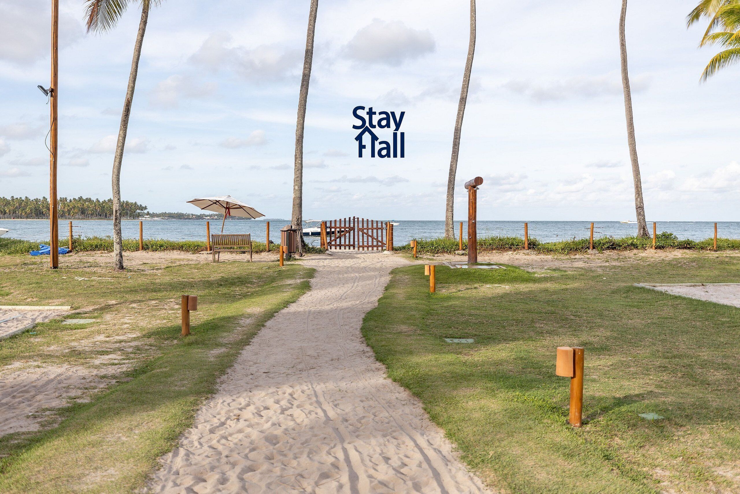 Un sentier menant à une plage bordée de palmiers, avec une porte en bois et un banc.